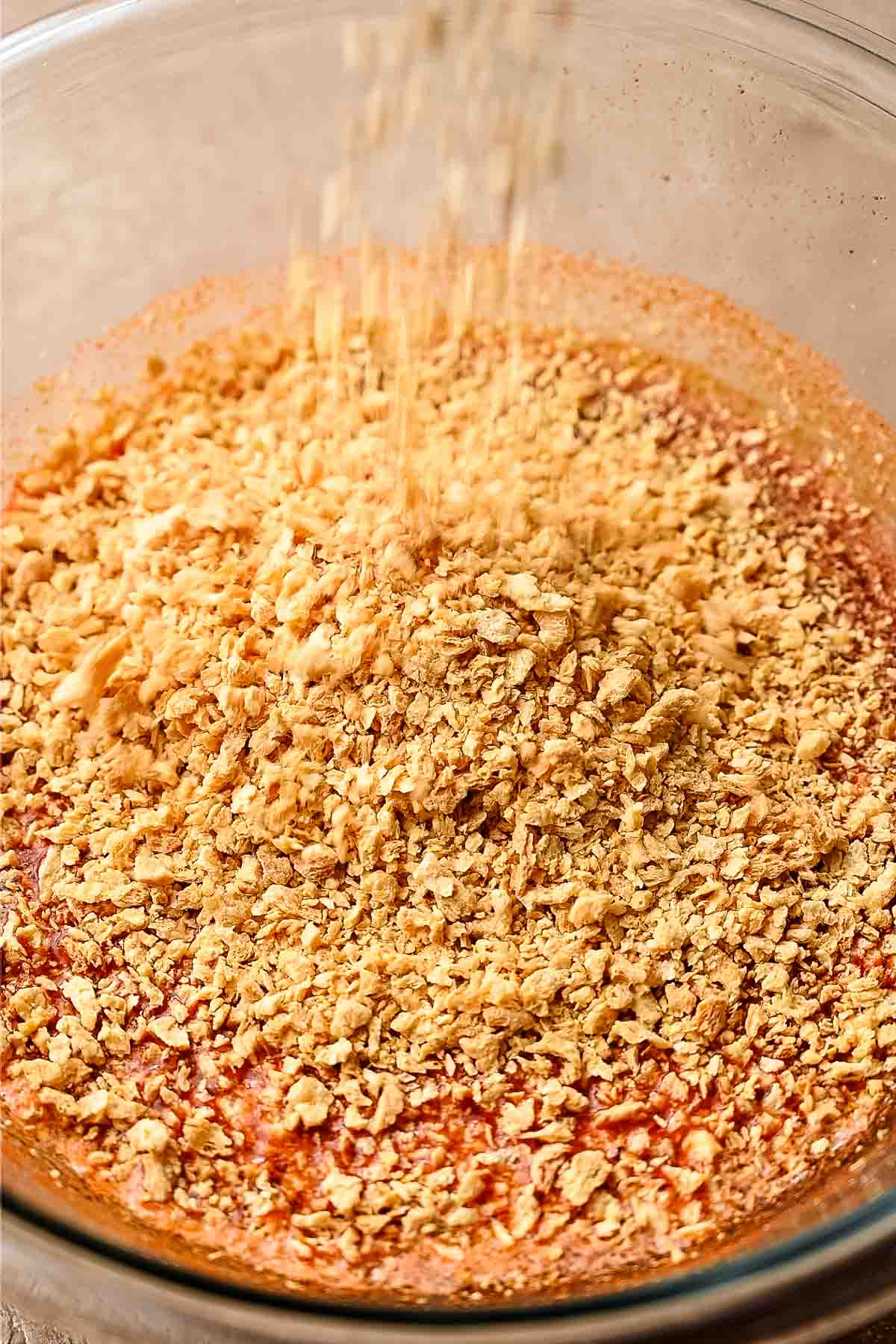 TVP being poured into a glass bowl with spices and veggie broth.
