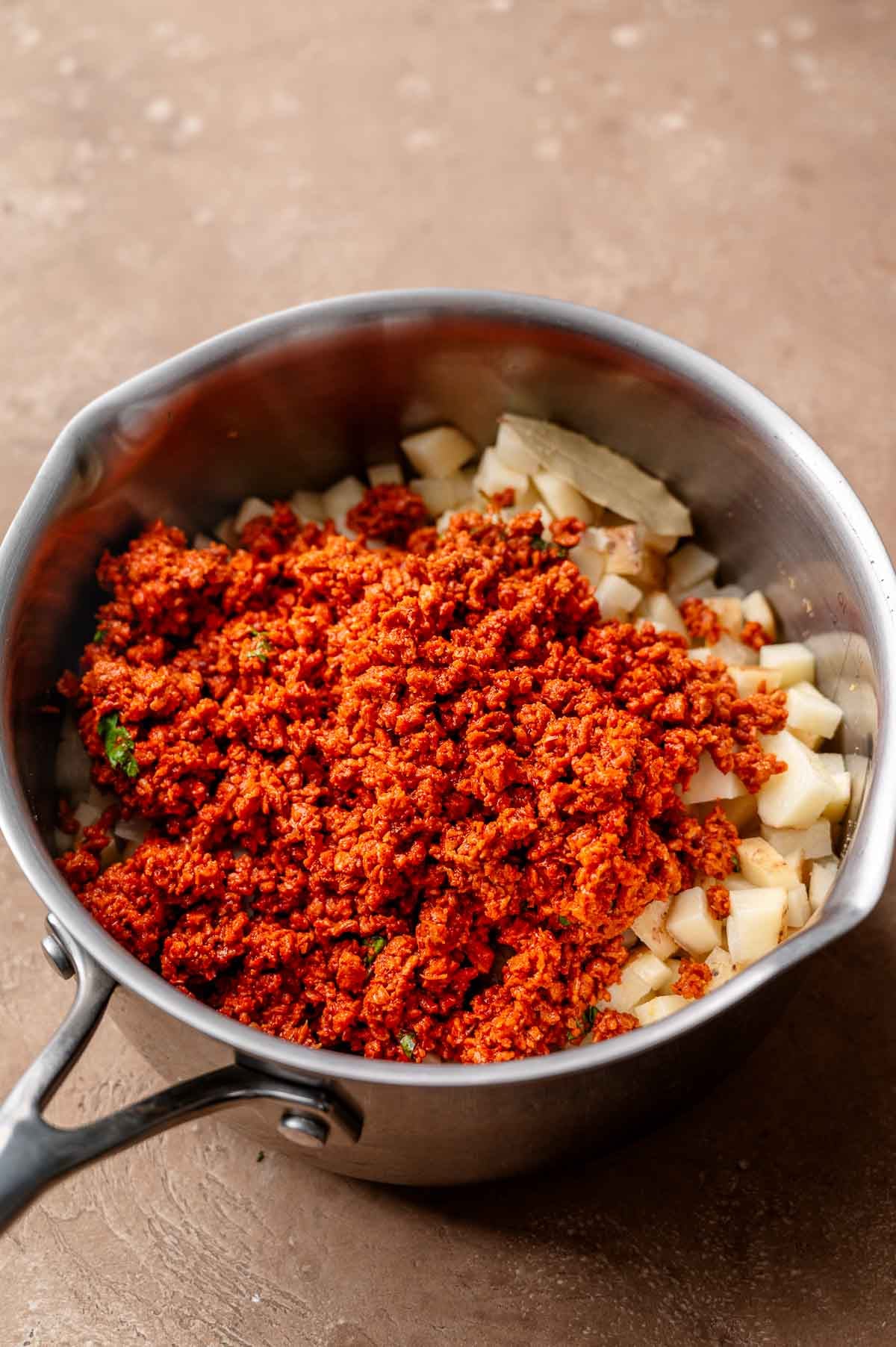 vegan chorizo on the diced potatoes in the stainless steel pot.