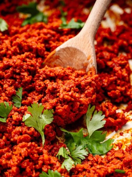 vegan chorizo on a wooden spoon with green cilantro leaves scattered on top.