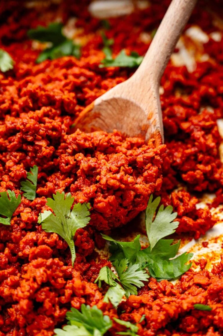 vegan chorizo on a wooden spoon with green cilantro leaves scattered on top.