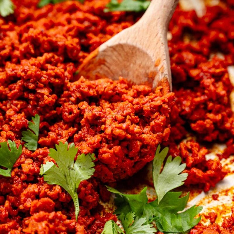 vegan chorizo on a wooden spoon with green cilantro leaves scattered on top.