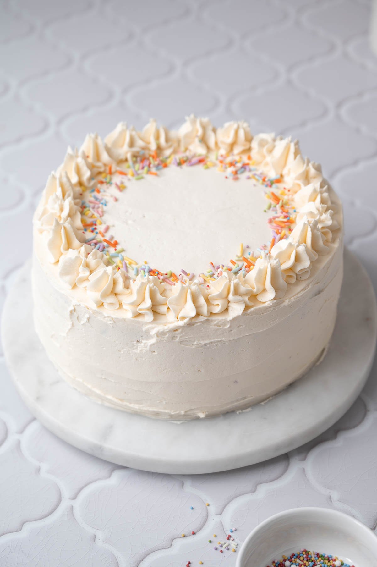 a frosted vegan vanilla layer cake with sprinkles on top.