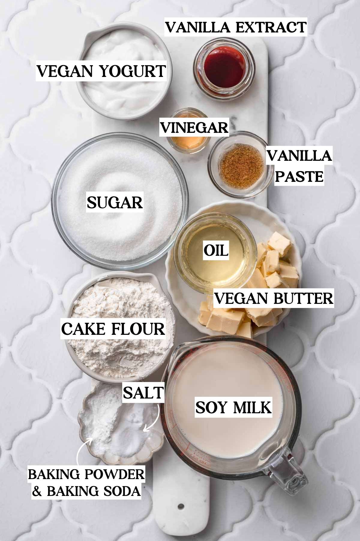 ingredients like cake flour, dairy free yogurt, sugar, vanilla extract and vanilla bean paste on a marble cutting board.
