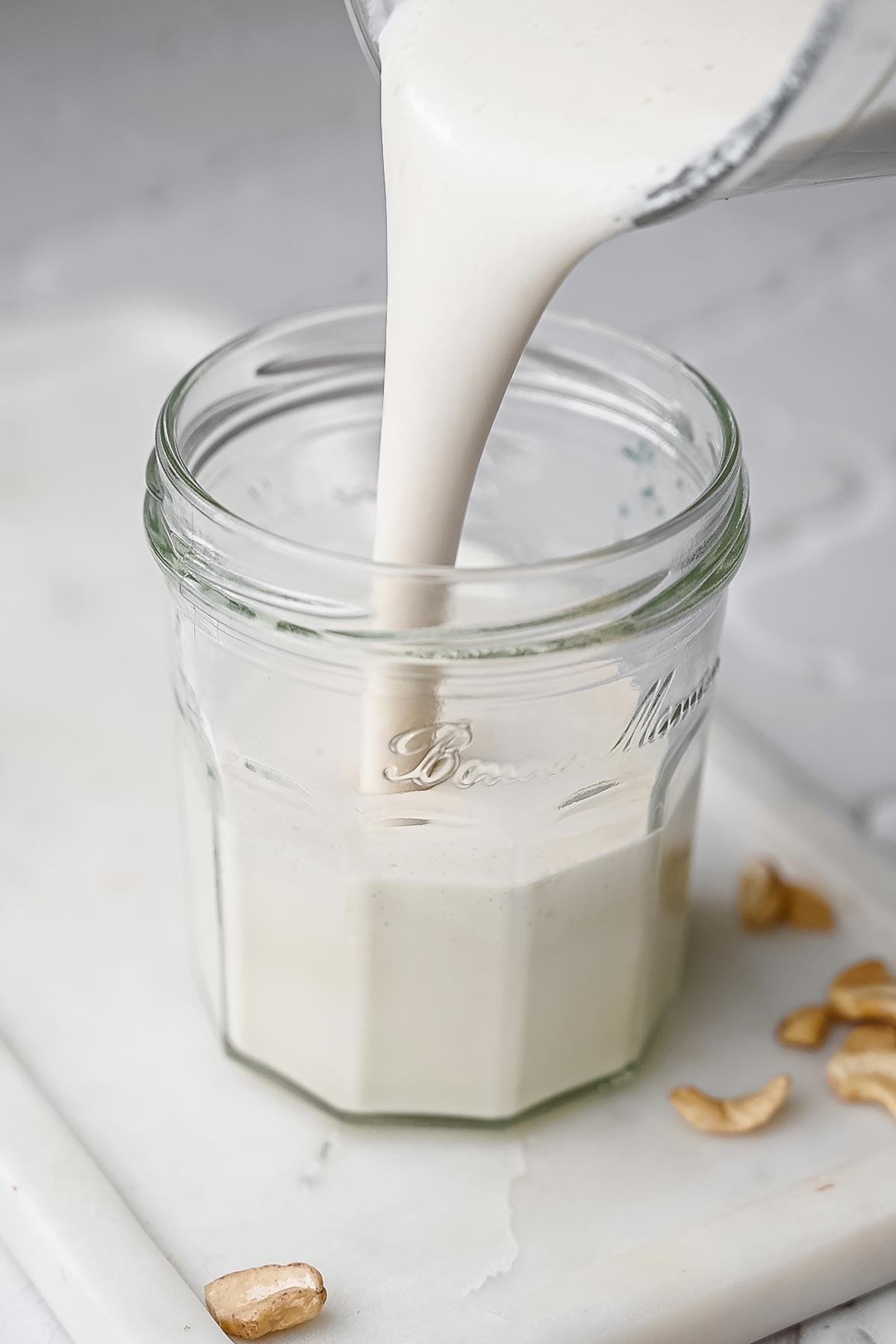 blended vegan sour cream being poured into a small glass jar.