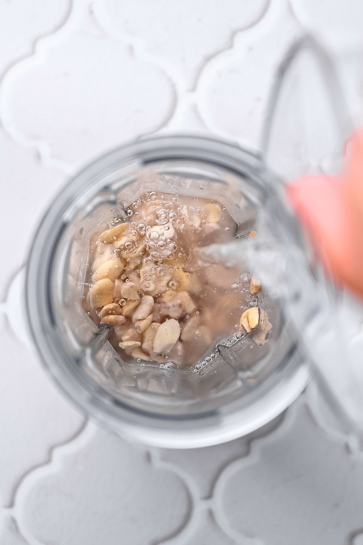 a hand pouring water into a single serve blender jar with soaked cashews.