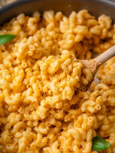 Close-up of creamy vegan mac and cheese with elbow pasta, coated in a rich, stretchy orange cheese sauce, stirred with a wooden spoon.