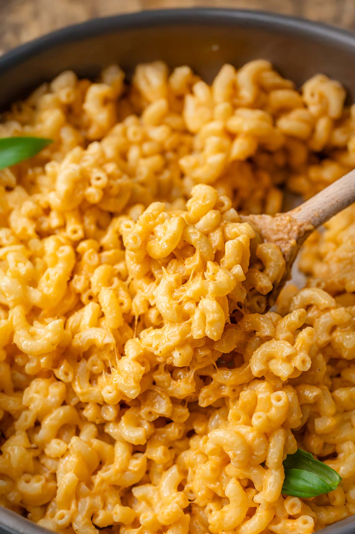 Close-up of creamy vegan mac and cheese with elbow pasta, coated in a rich, stretchy orange cheese sauce, stirred with a wooden spoon.