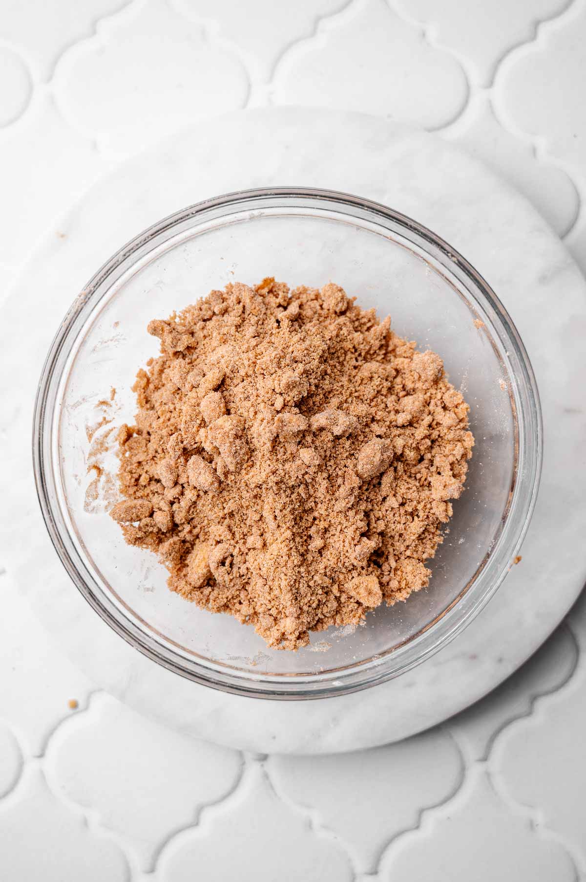 Bowl of cinnamon sugar crumble mixture for vegan coffee cake muffins, showing a coarse, sandy texture.