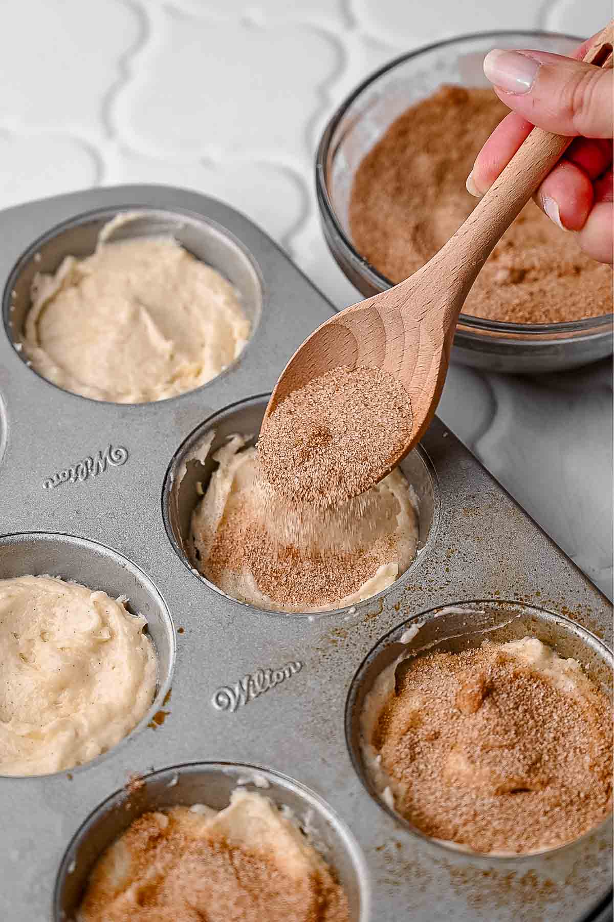 Muffin tin filled with batter and topped with cinnamon sugar mixture before baking.