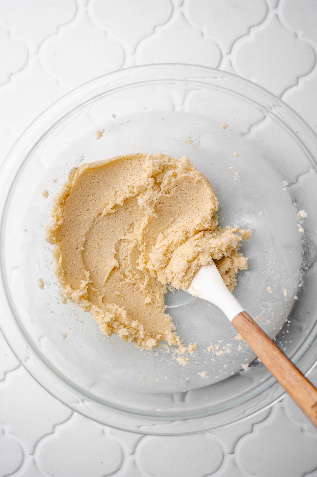 Bowl with creamed vegan butter and sugar mixture being mixed with a spatula until light and fluffy.