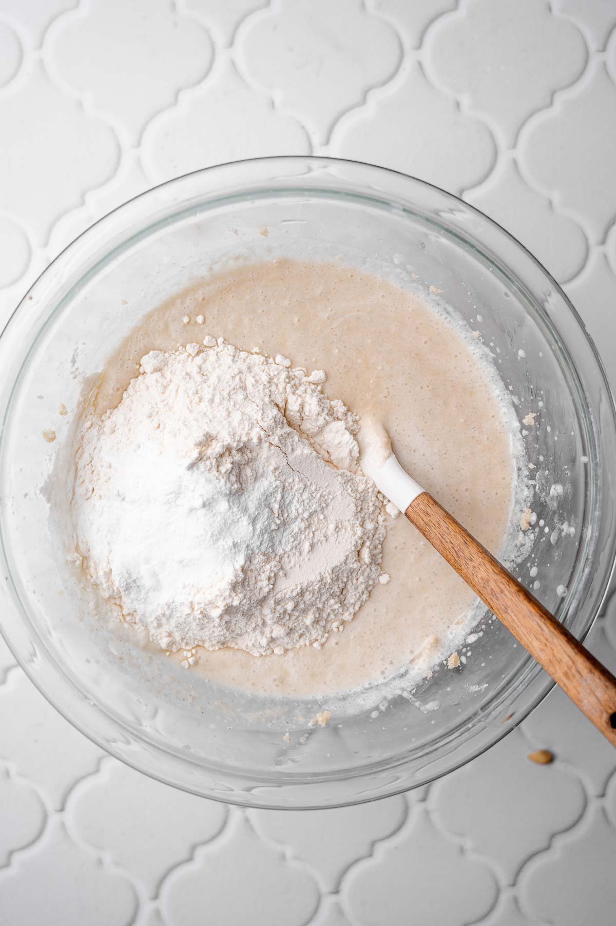 Dry ingredients like flour, baking powder, and salt being added to wet mixture in a glass bowl for muffin batter.