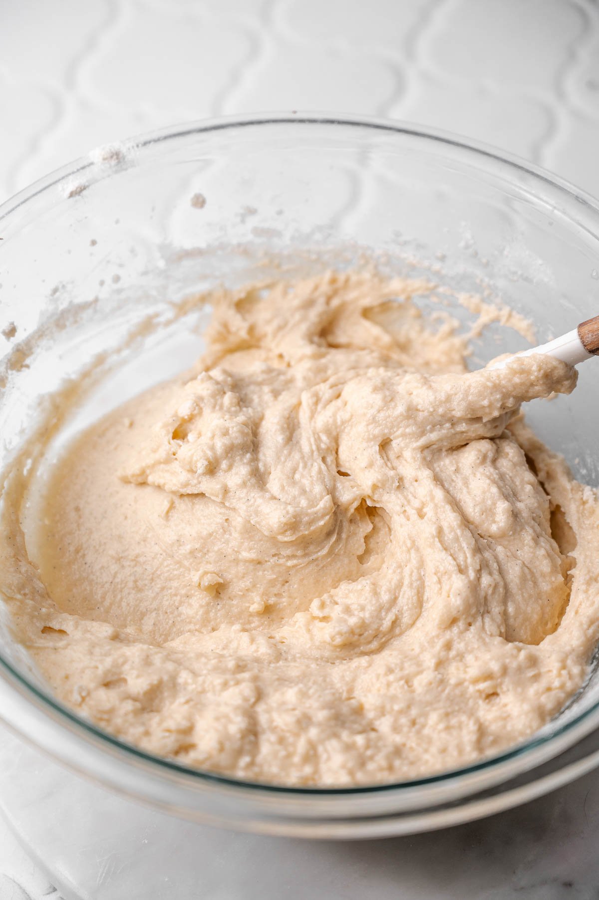 Smooth, thick vegan coffee cake muffin batter being gently folded together in a glass bowl.