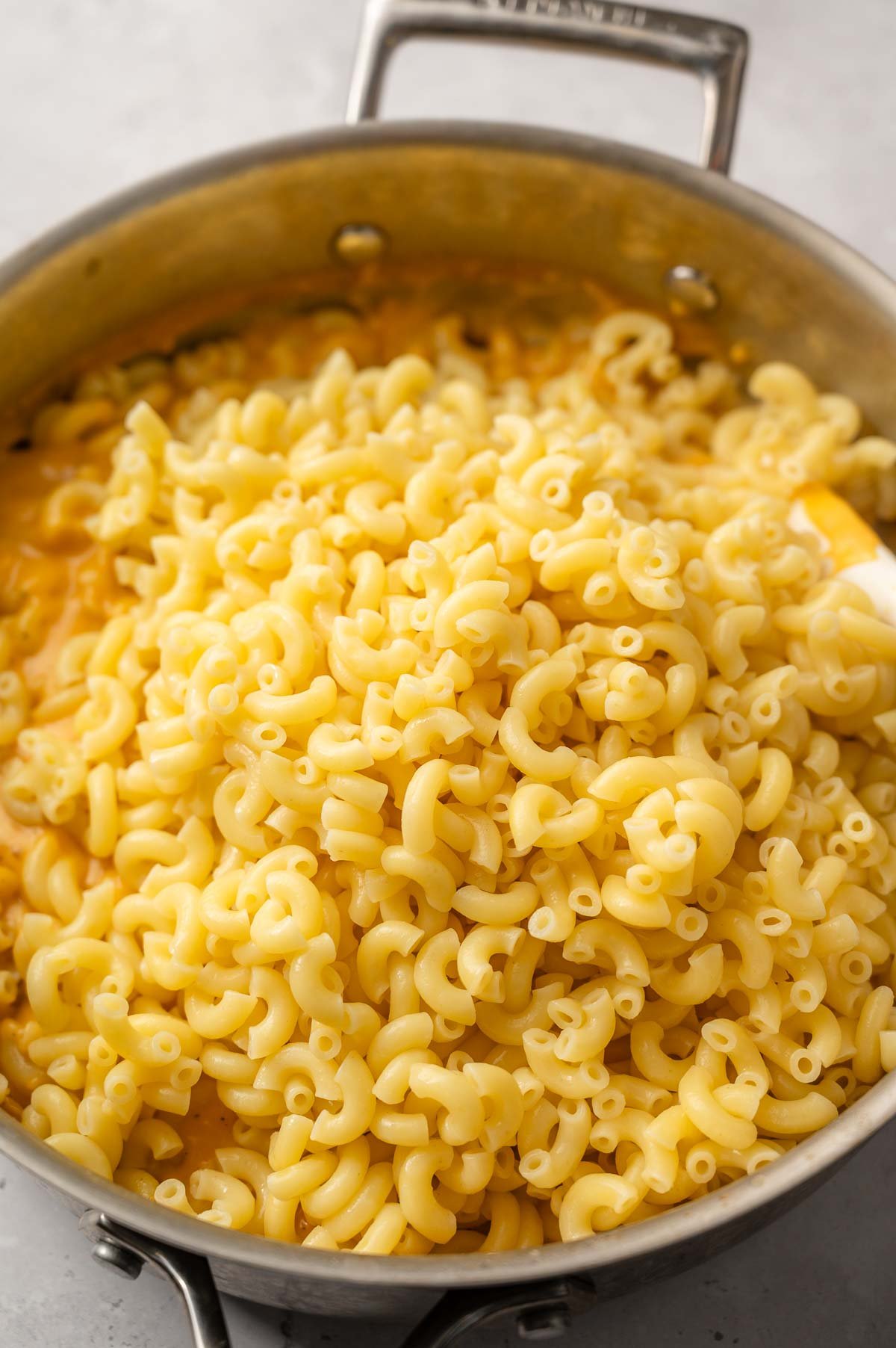 cooked macaroni pasta added to the vegan cheese sauce in a pan.