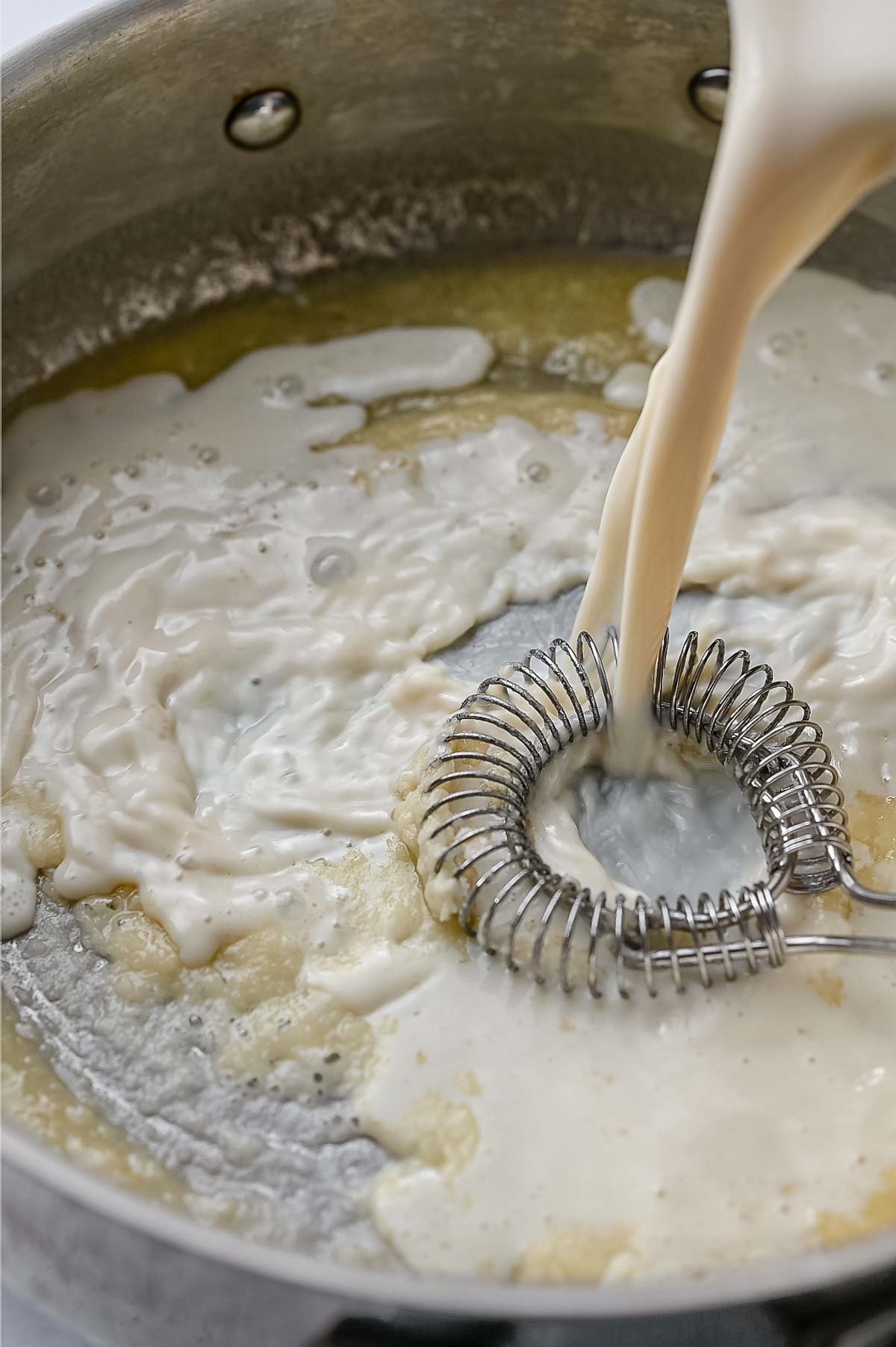 Pouring soy milk into the roux while whisking.