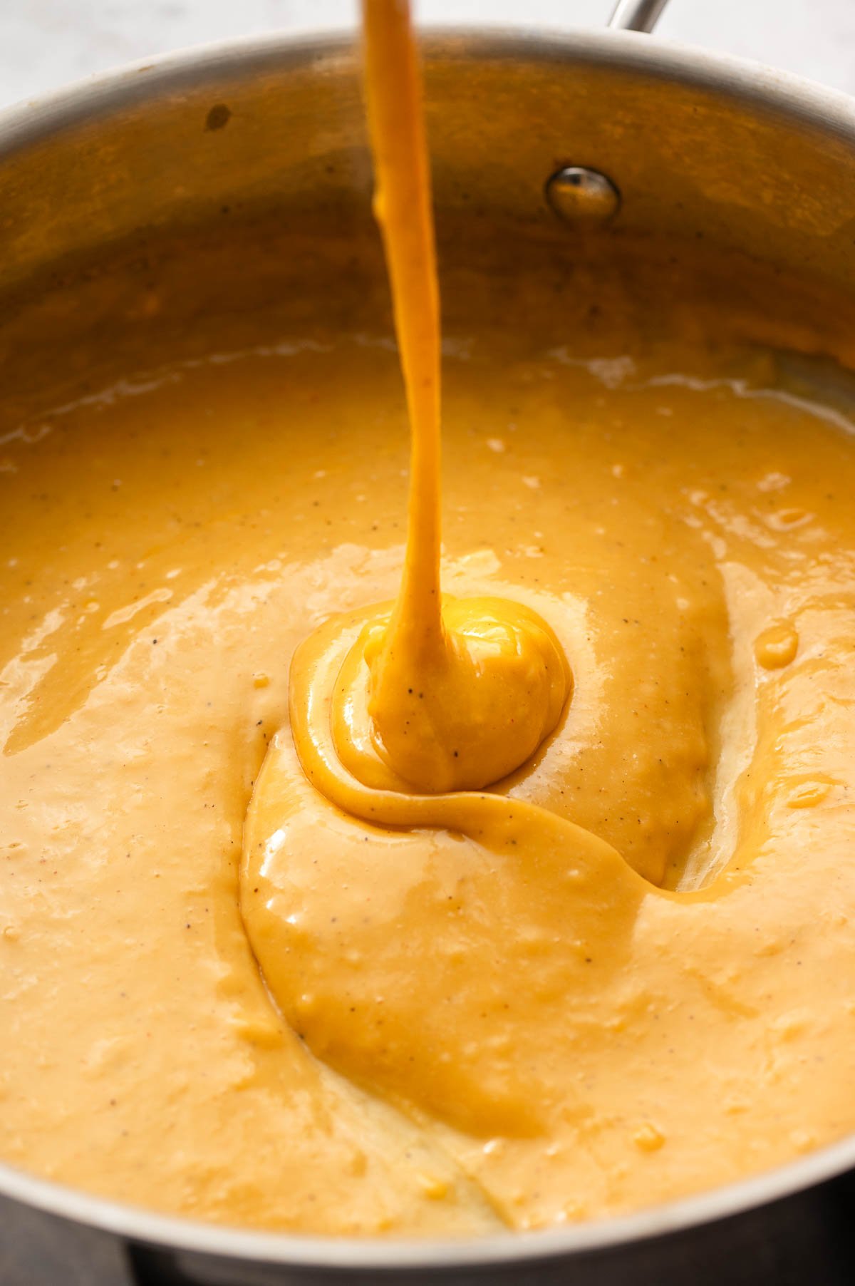 Stretchy orange vegan cheese sauce dripping from a spoon.
