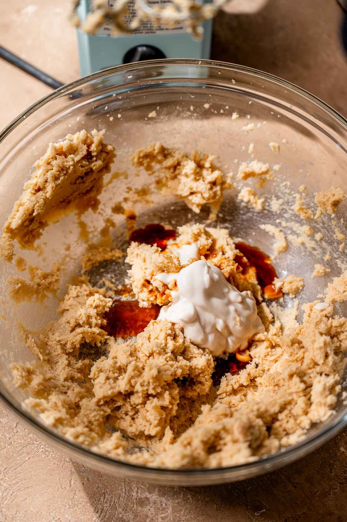 Creamy vegan butter mixture in a bowl with added vanilla extract and dairy-free yogurt.