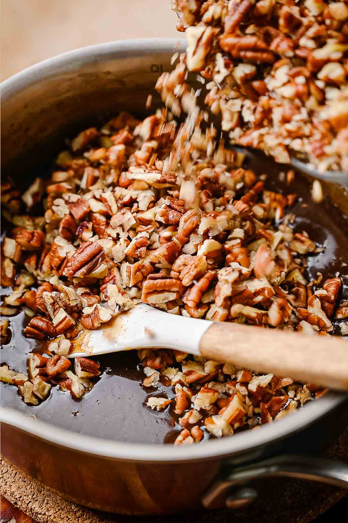 Chopped pecans being poured into a saucepan of warm vegan pecan pie filling and stirred together with a spatula.