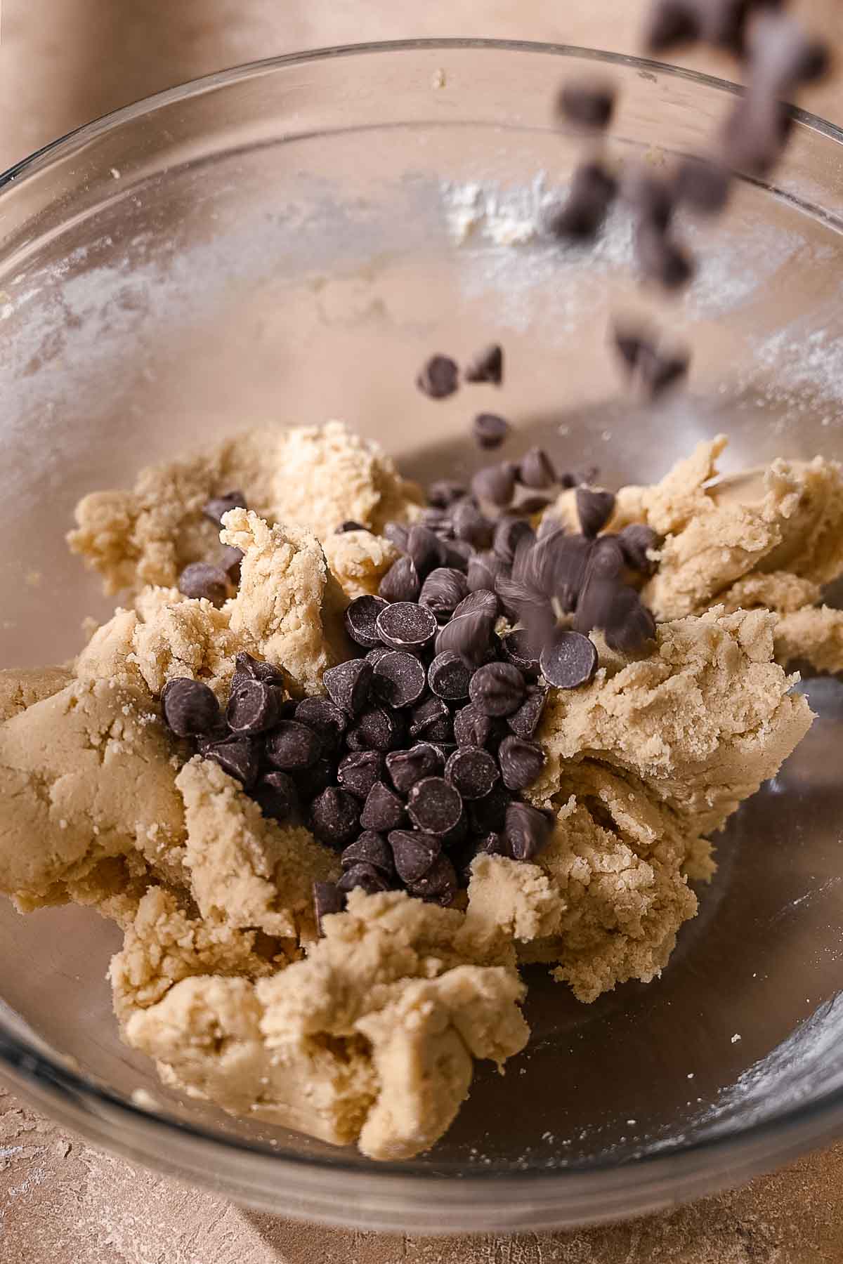 Pouring dairy-free chocolate chips into a bowl of vegan cookie dough.