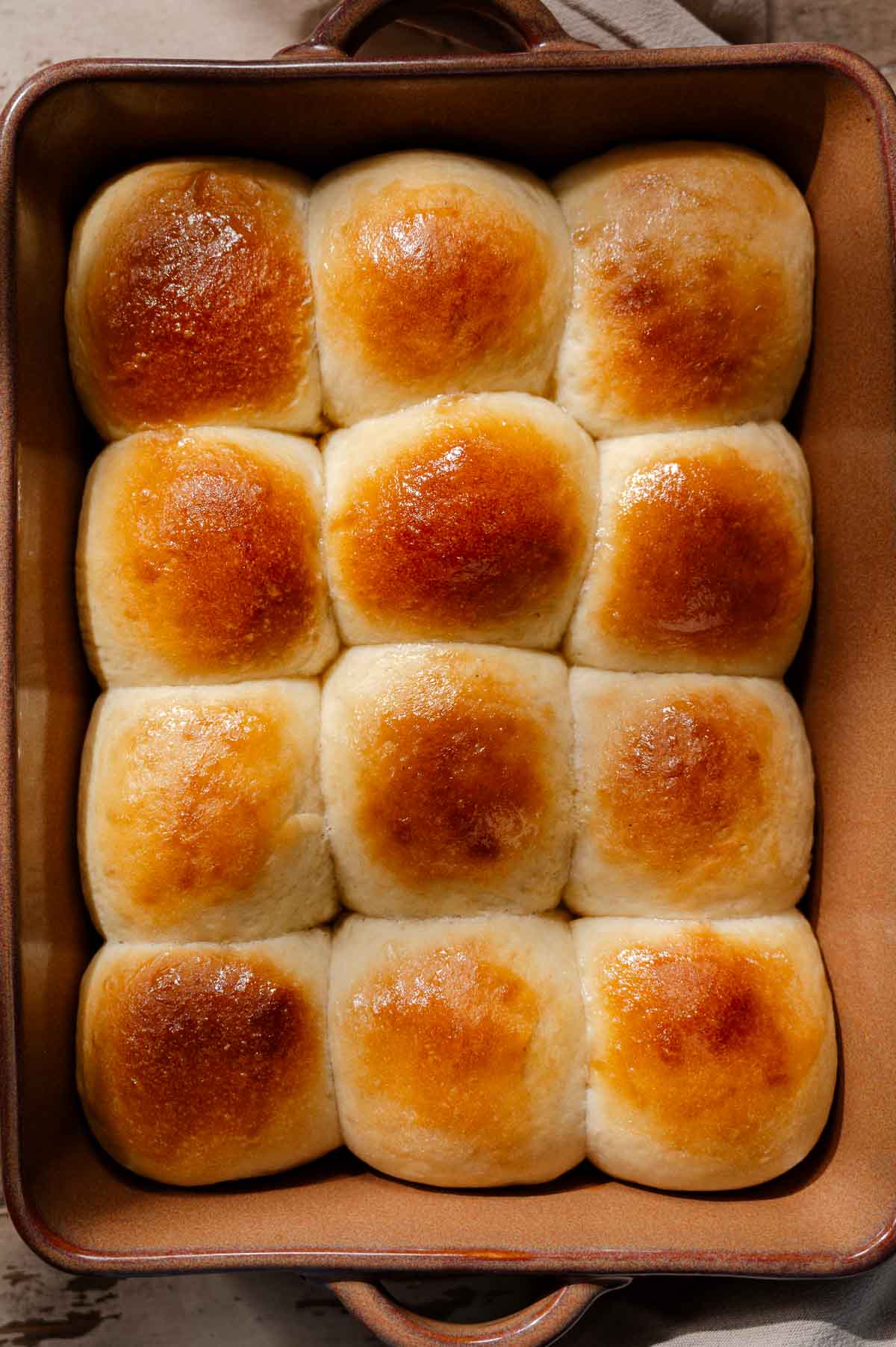 a tray of golden brown baked vegan dinner rolls with a shiny exterior. 