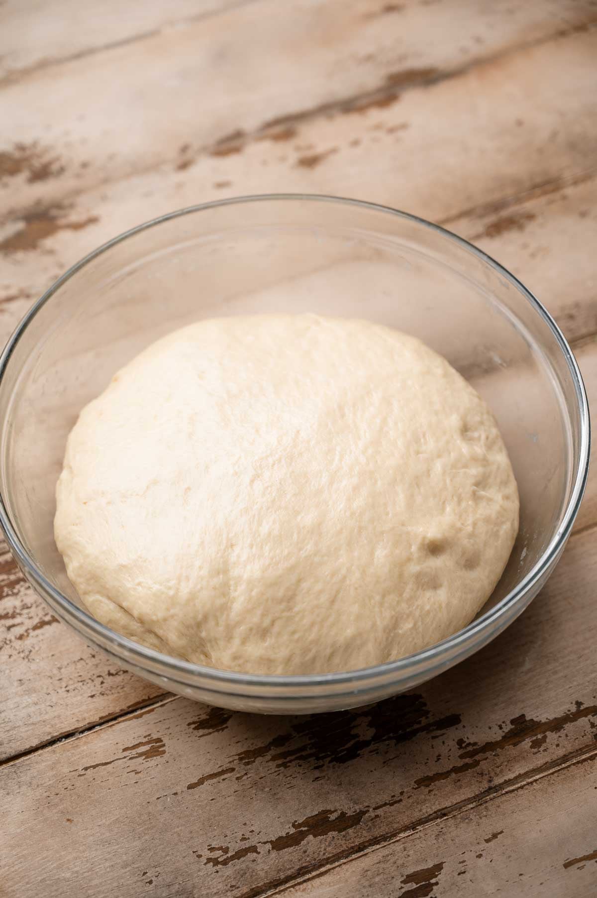 the risen vegan dinner roll dough ball in a glass bowl.
