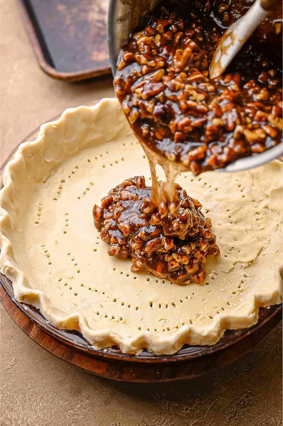 Gooey vegan pecan pie filling being poured from a saucepan into an unbaked pie crust that has been docked with a fork.