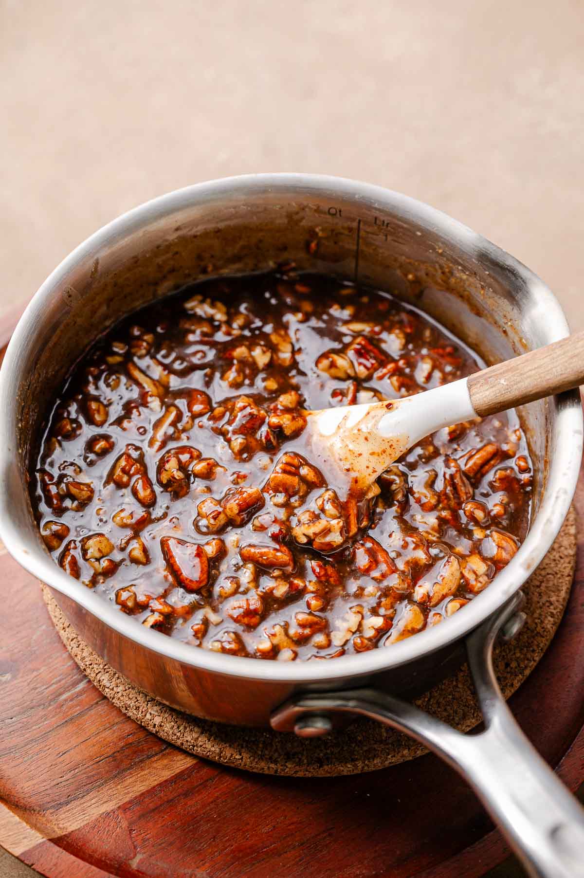 A saucepan filled with mixed vegan pecan pie filling, showing chopped pecans coated in glossy, caramel-style custard.