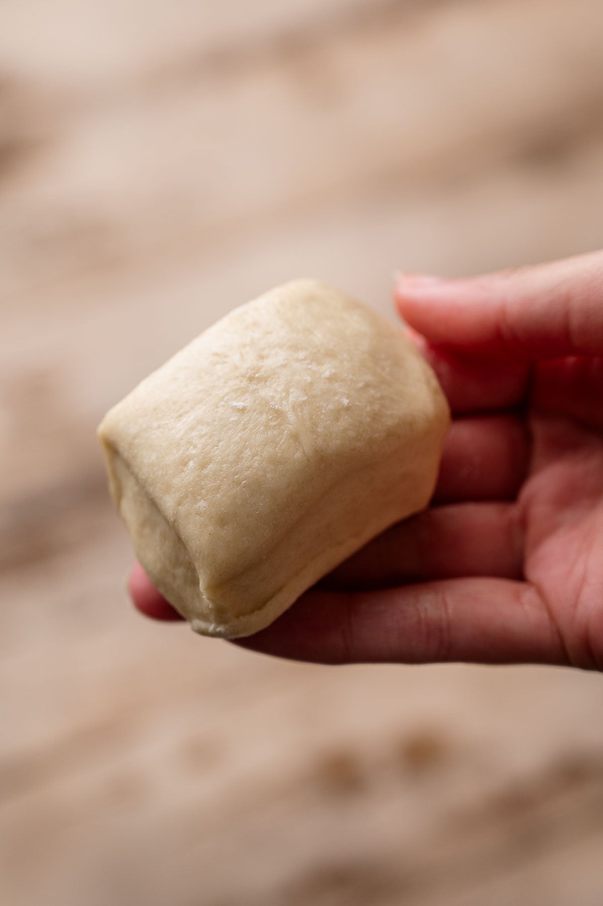 a hand holding a small, cut portion of the dough, ready to be rolled.