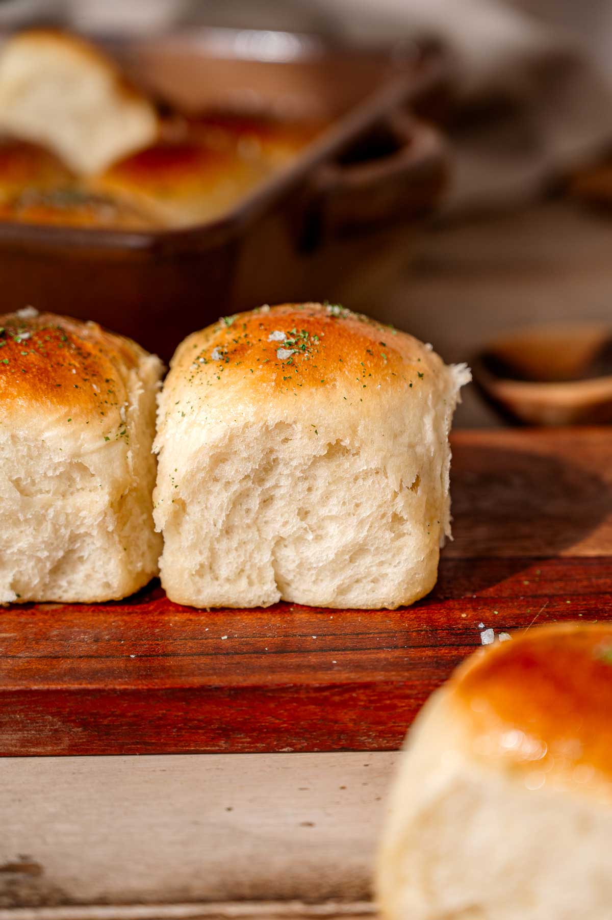 two vegan dinner rolls on a wooden cutting board with the soft, fluffy texture of the sides exposed.