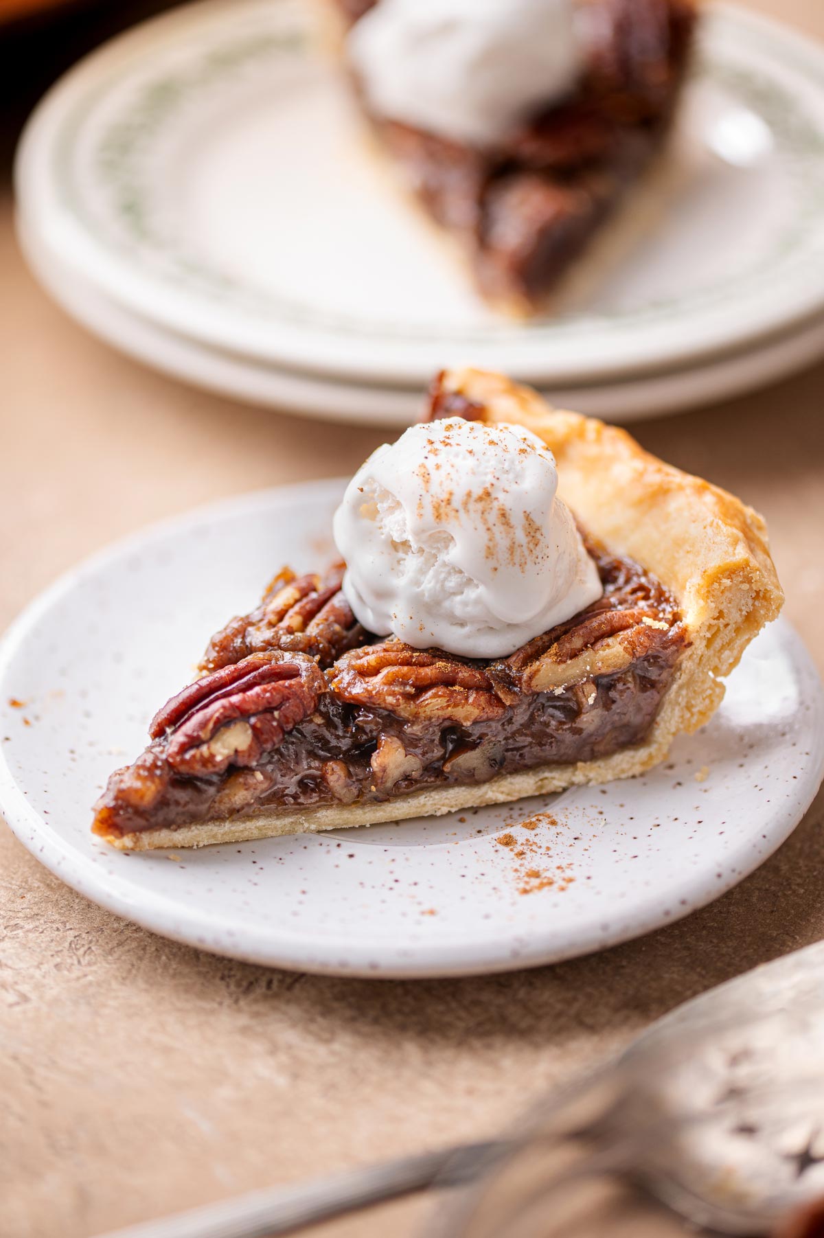 A slice of gooey vegan pecan pie on a white plate with a scoop of dairy-free ice cream on top.