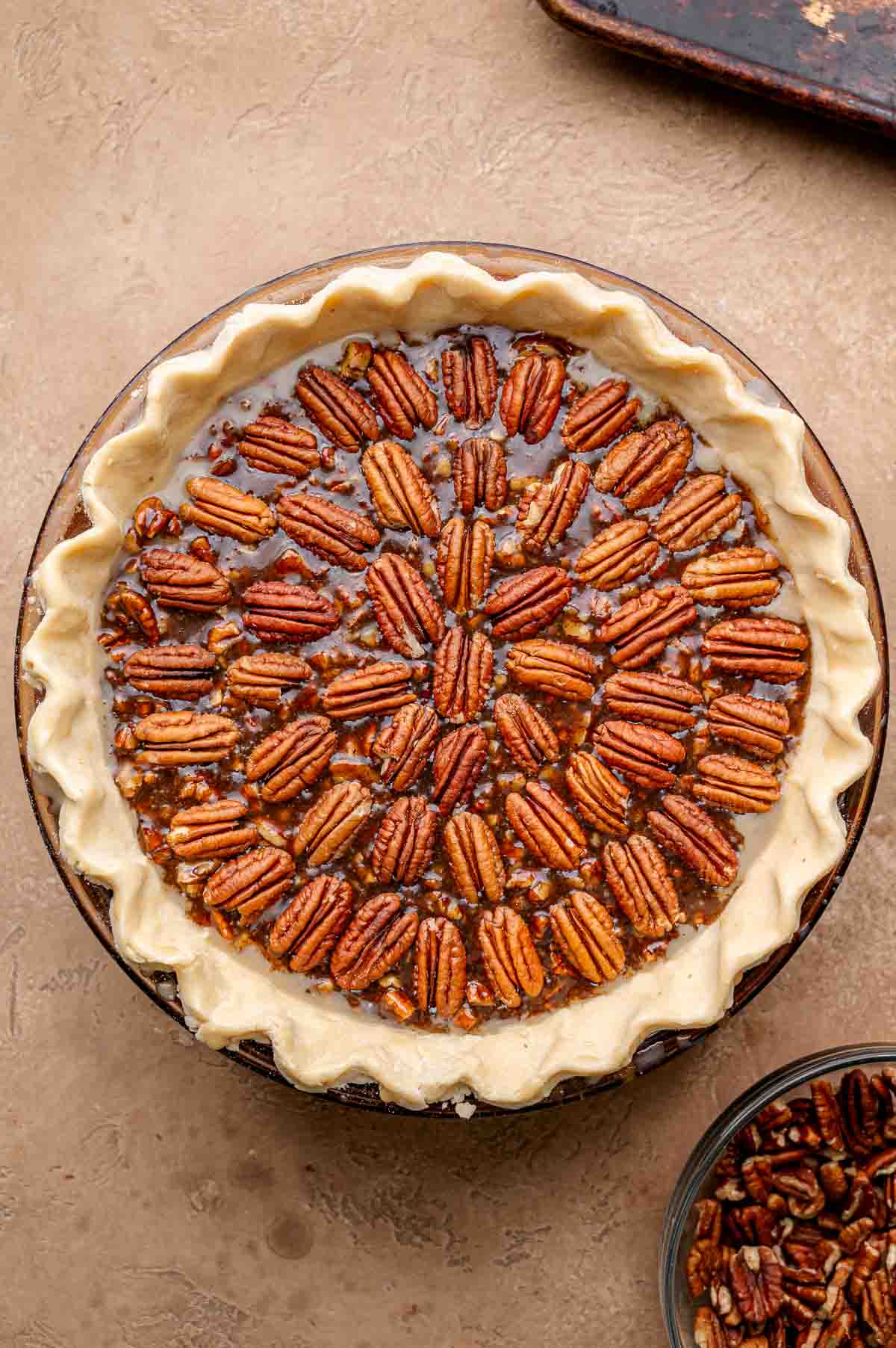 Unbaked vegan pecan pie with pecans neatly arranged in a circular pattern on top of the filling inside a raw pie crust.