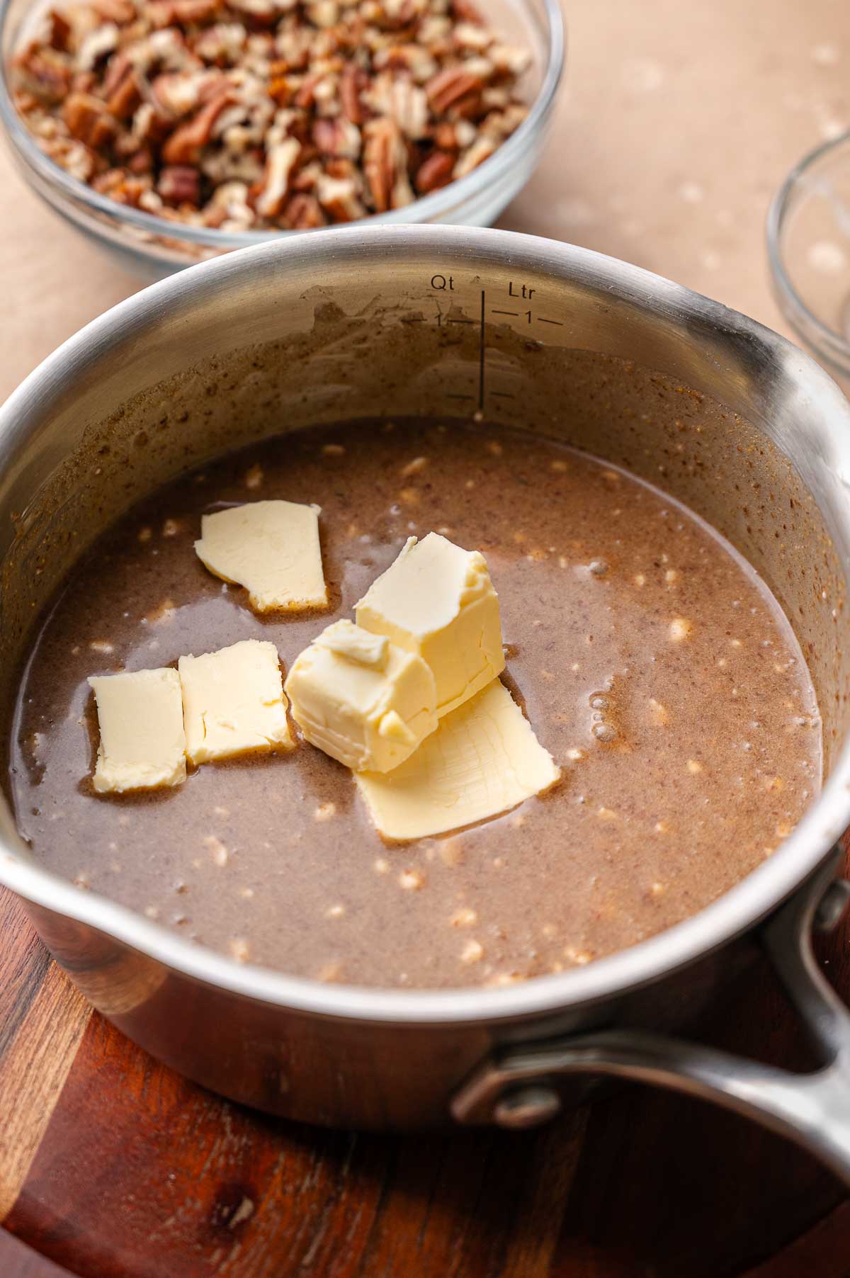 Several cubes of vegan butter melting into a pot of brown sugar, maple syrup, and coconut milk pecan pie custard.
