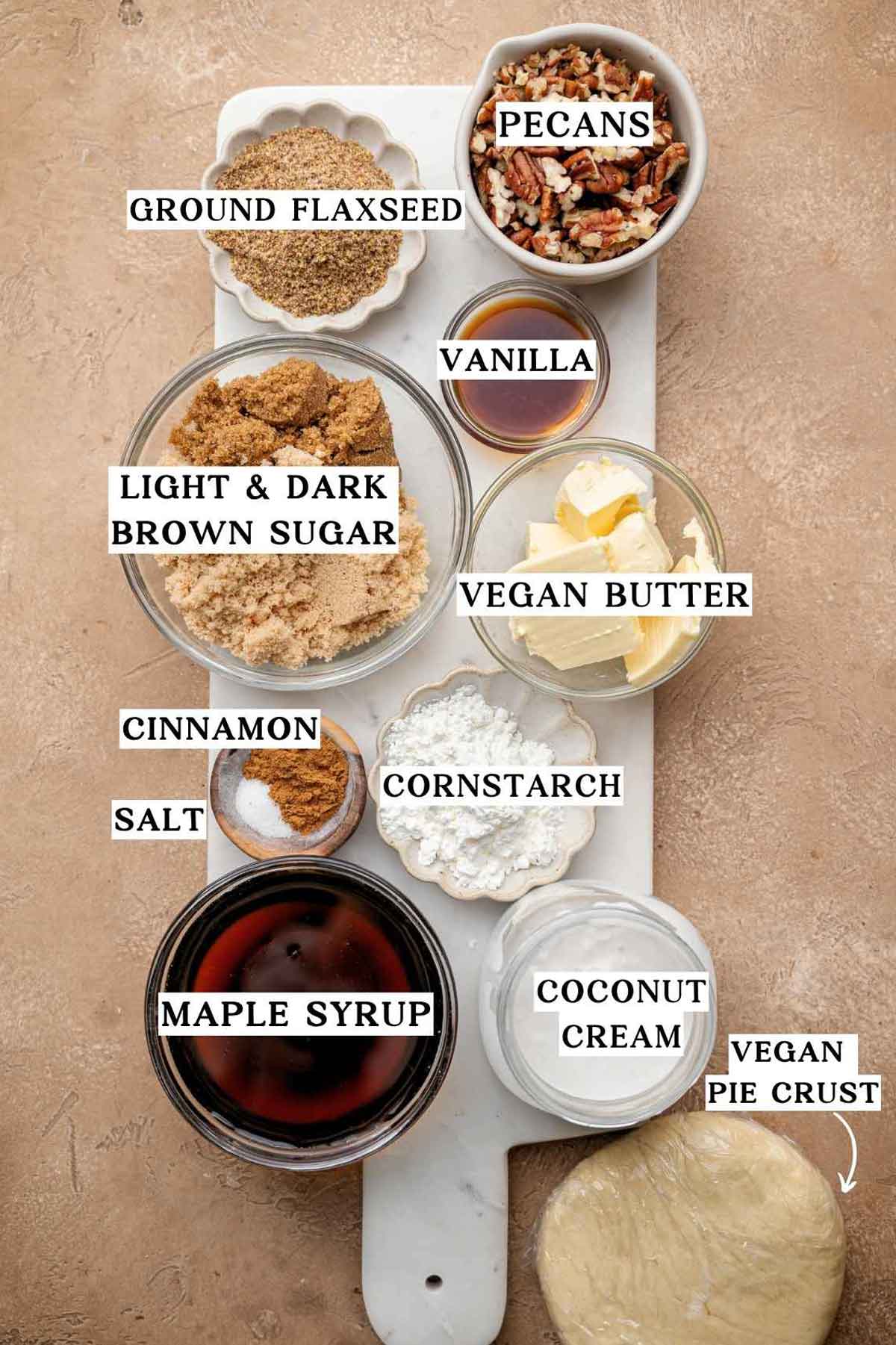 Overhead view of vegan pecan pie ingredients including brown sugar, maple syrup, coconut cream, pecans, cornstarch, vegan butter, ground flaxseed, cinnamon, salt, and pie dough.