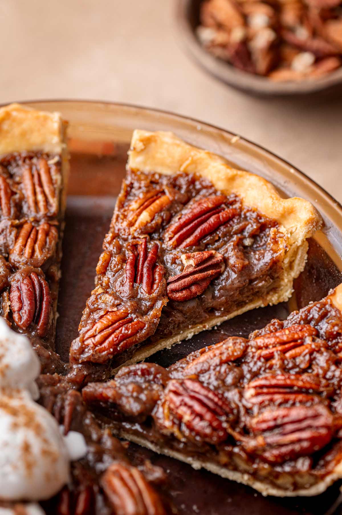 A close-up slice of vegan pecan pie with toasted pecans on top and a flaky pie crust.