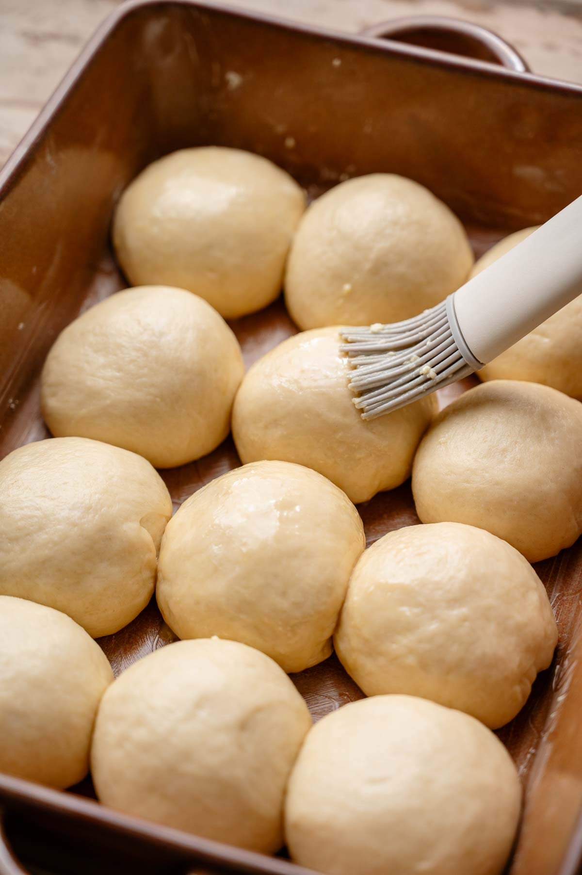 a gray brush coating the unbaked vegan rolls with an eggless egg wash.
