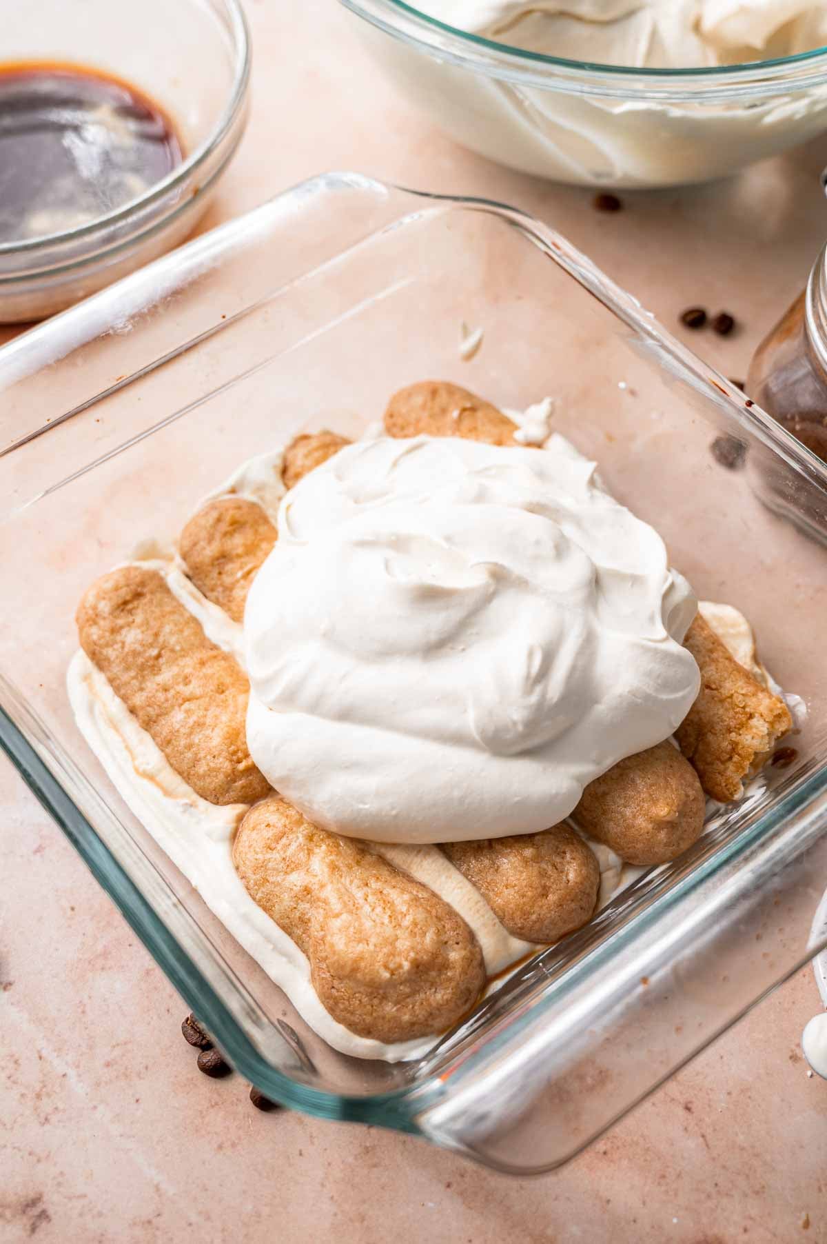 eight soaked vegan ladyfingers in a glass pan with a dollop of vegan mascaarpone on top.