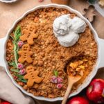 a white baking dish with a vegan apple crisp topped with gingerbread crumble.