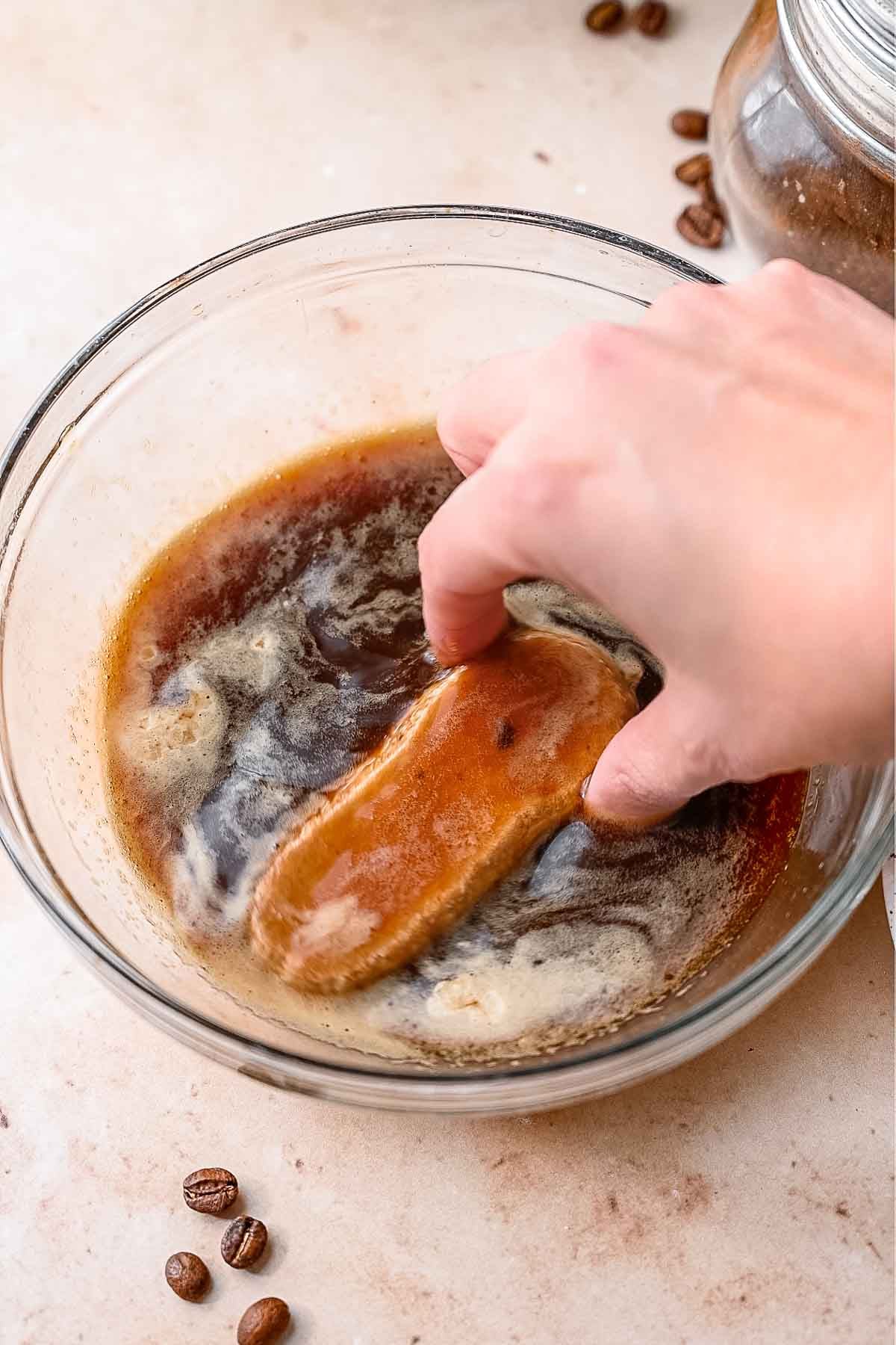 a hand dipping a ladyfinger in espresso.