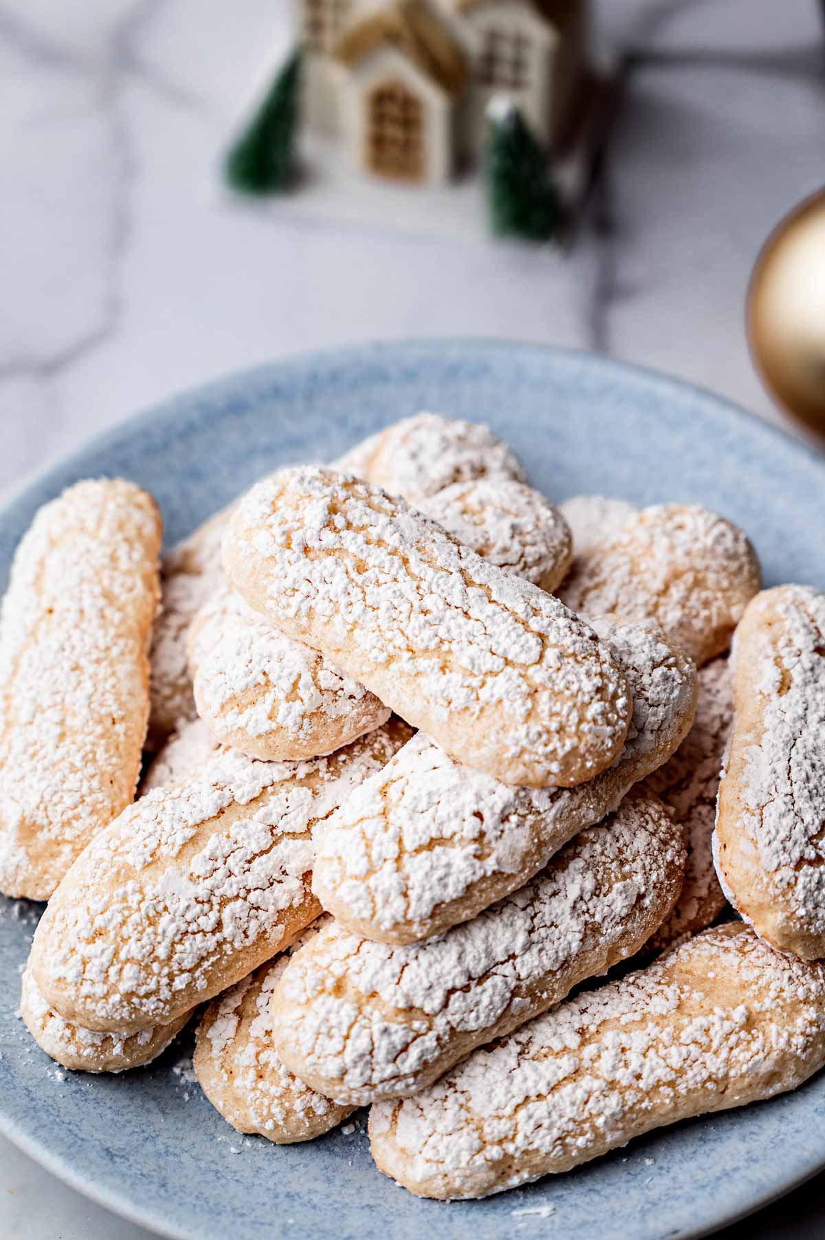 Finished vegan ladyfinger cookies dusted with powdered sugar and stacked on a blue plate.