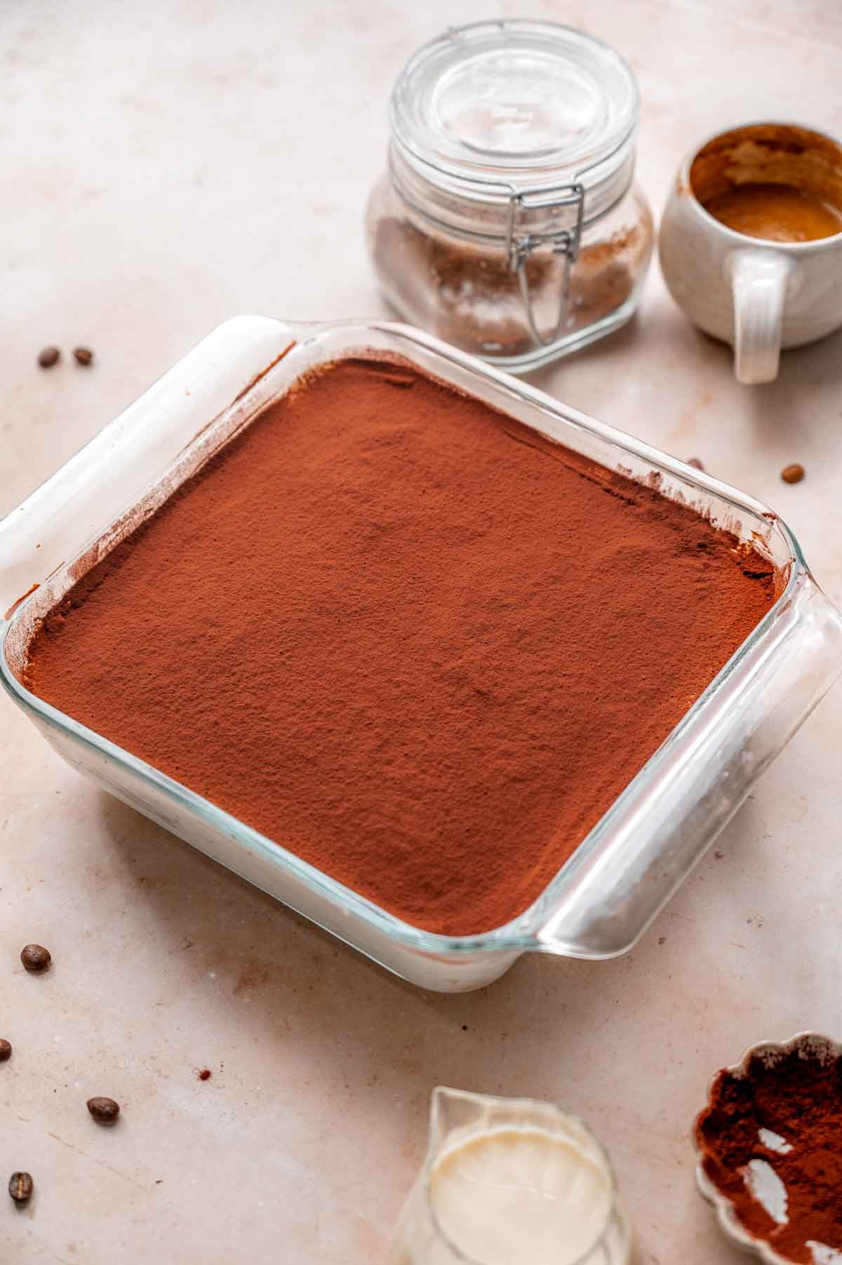 a glass pan of vegan tiramisu with a dusting of cocoa powder on top.