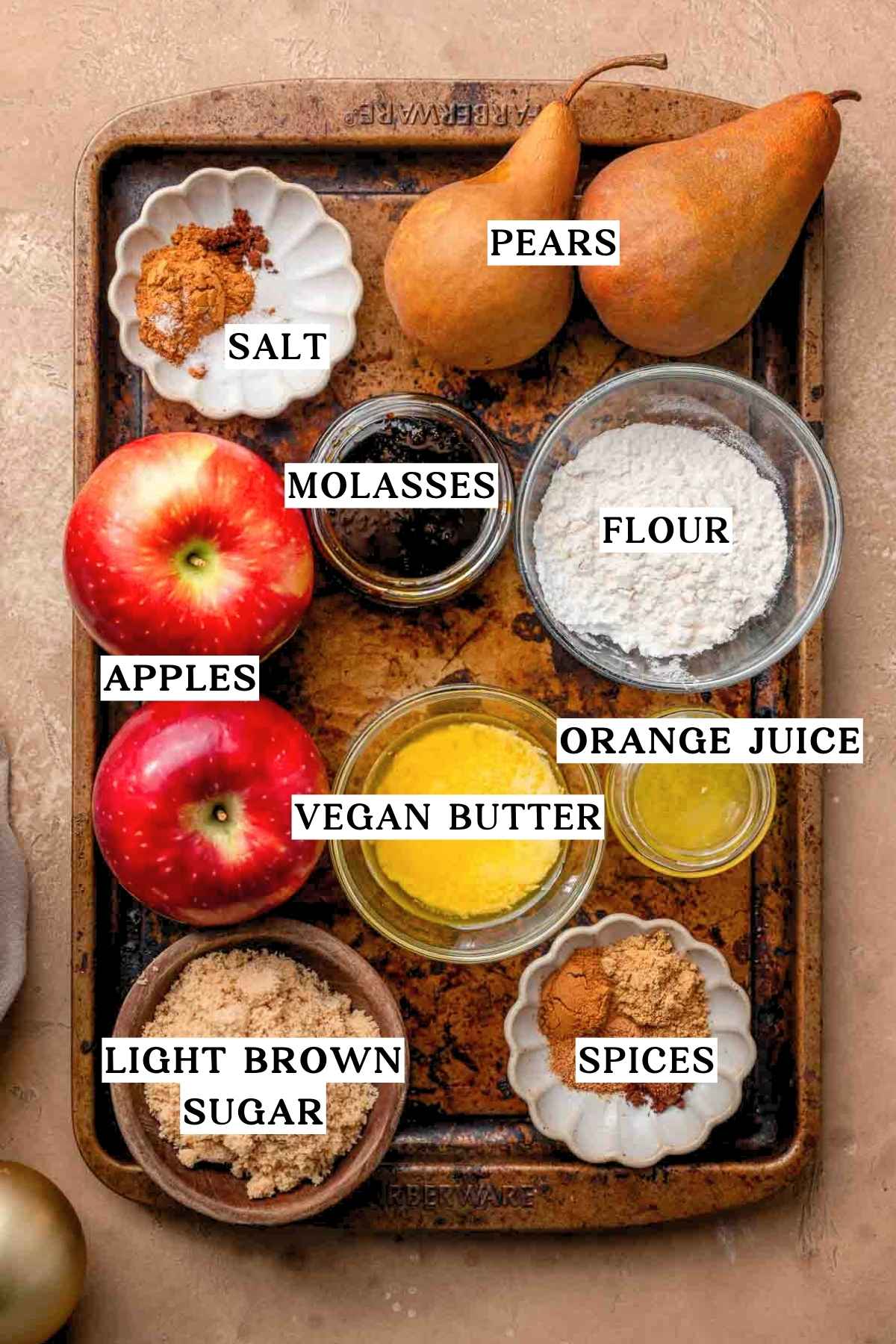 ingredients like apples, bosc pears, melted vegan butter, flour and spices on a dark metal pan.