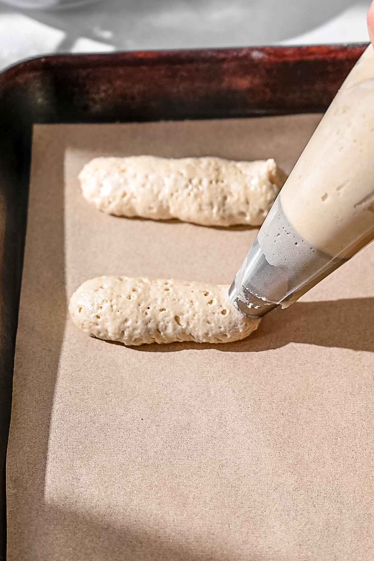 Unbaked vegan ladyfinger cookies piped onto a parchment-lined baking sheet.