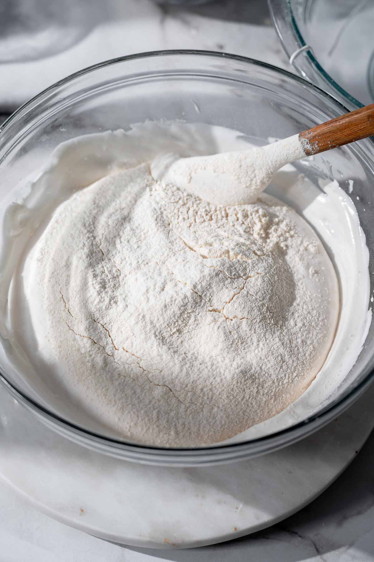 Sifted flour added over whipped aquafaba during the ladyfinger batter mixing process.