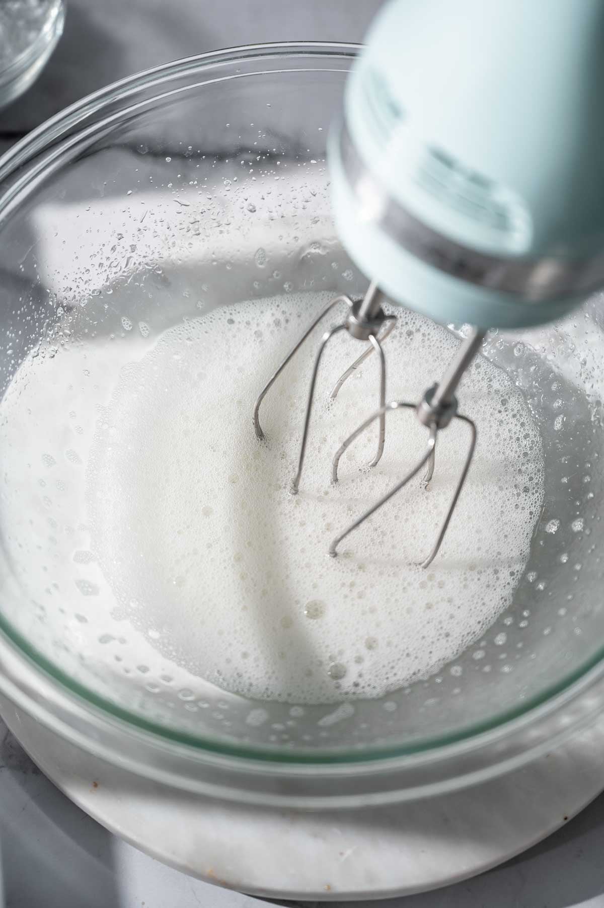 Aquafaba being whipped with a hand mixer in a glass bowl to create a vegan egg white foam.
