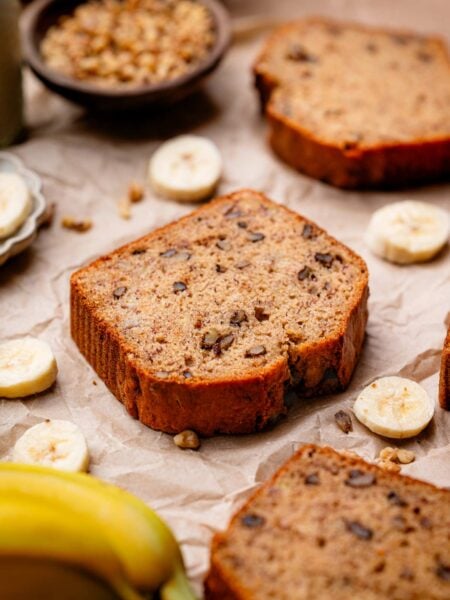 a slice of vegan banana bread with walnuts on a crumpled brown parchment.