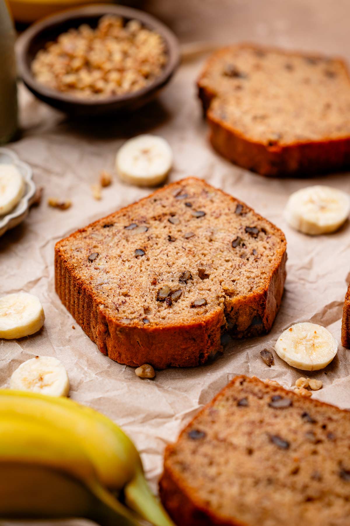 a slice of vegan banana bread with walnuts on a crumpled brown parchment.