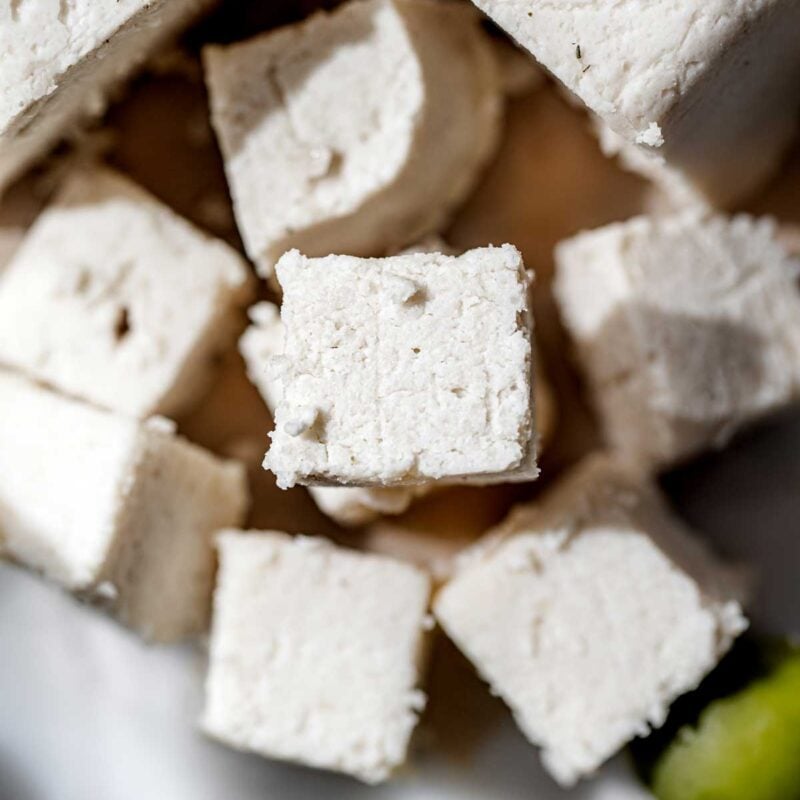 Close-up of homemade vegan feta cheese cut into rustic cubes, showing a crumbly texture and clean edges.