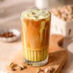 an iced pistachio latte with oatmilk on a wood cutting board.