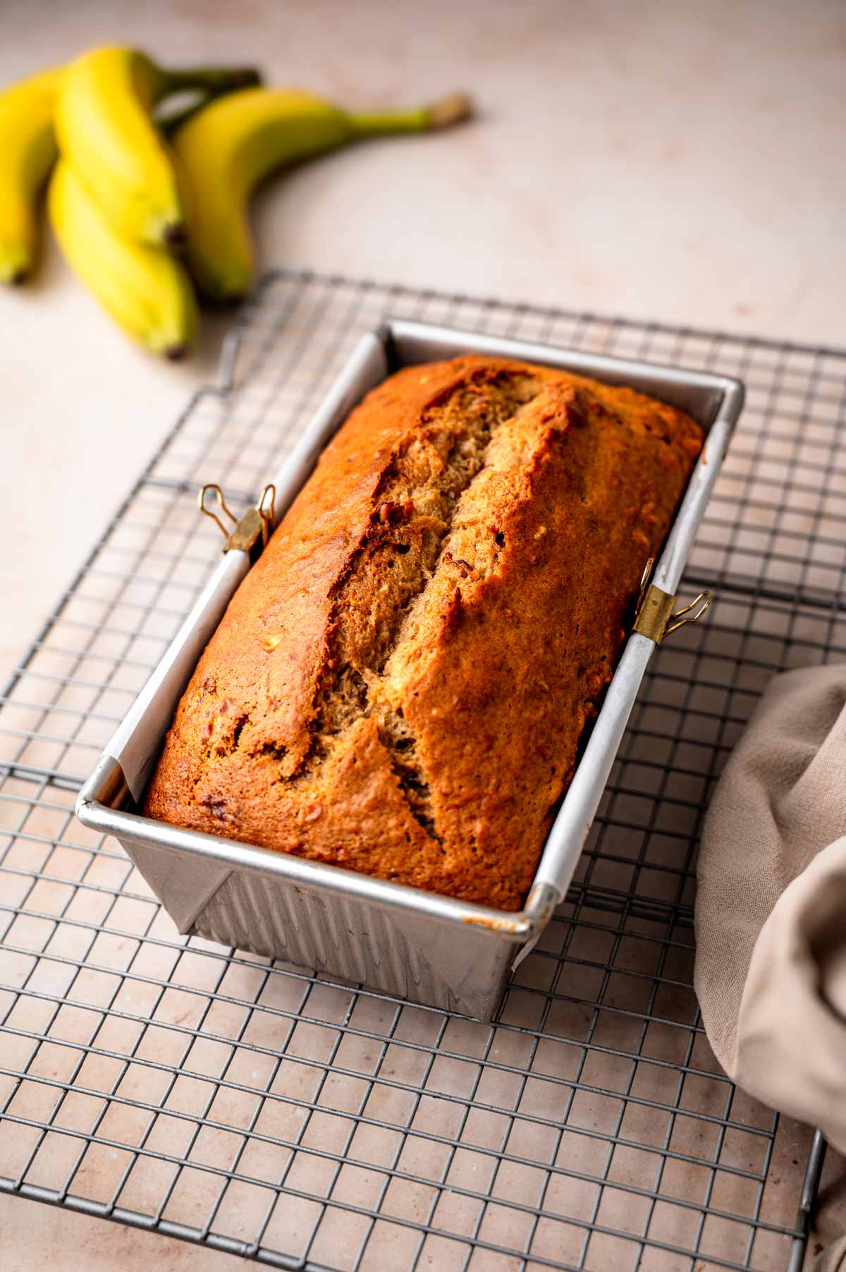 the baked vegan banana bread loaf in a pan on a wire cooling rack.