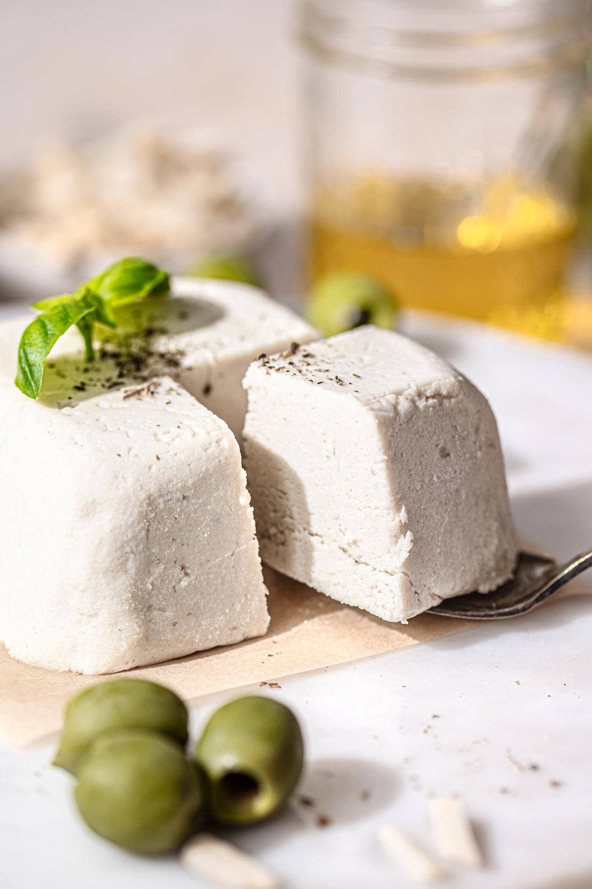 a block of vegan feta with a slice taken out on brown parchment paper before slicing.