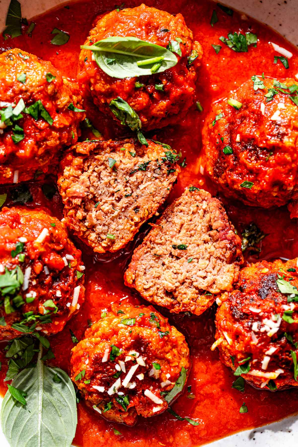 Close-up of vegan meatballs in marinara sauce with one meatball cut open to show a tender, meaty texture inside.